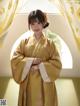 A woman in a yellow kimono standing in front of a window.