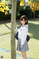 A woman in a school uniform leaning against a tree.