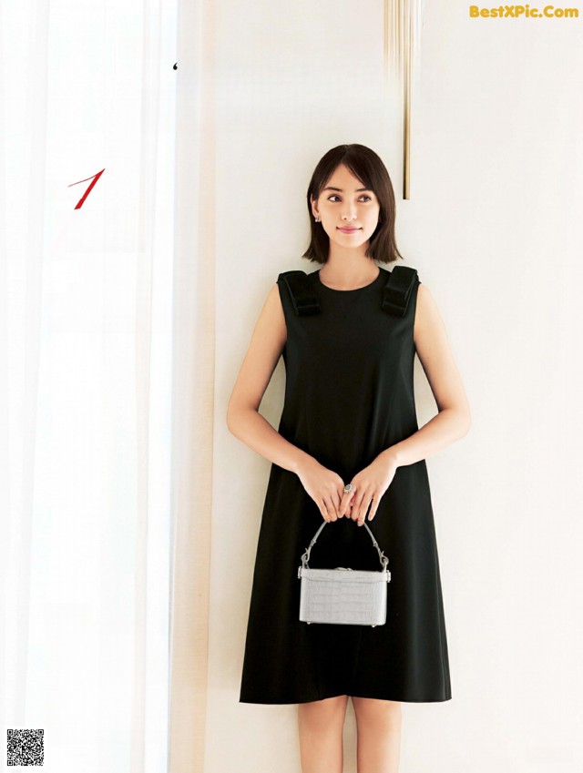 A woman in a black dress holding a white purse.