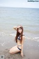 A woman in a blue bikini sitting on the beach.