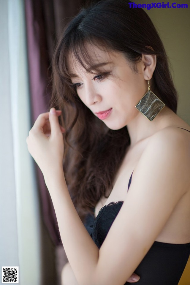 A woman in a black dress leaning against a window.