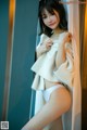 A woman in a white underwear leaning against a curtain.