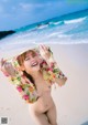 A naked woman standing on a beach next to the ocean.