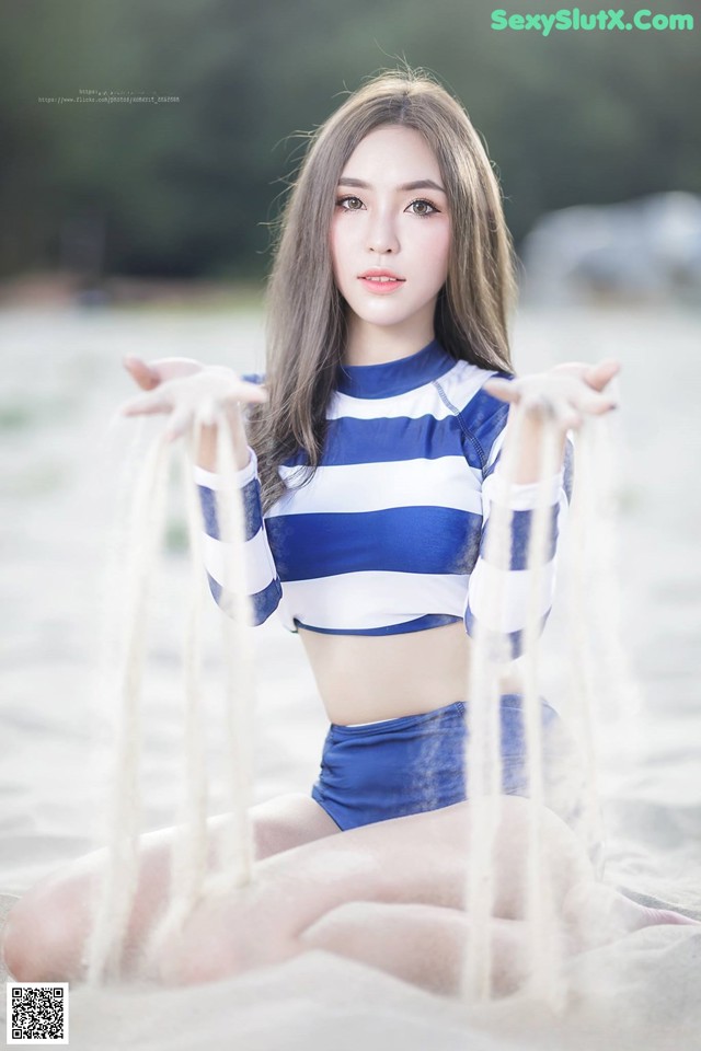 A woman in a blue and white striped top sitting on a beach.